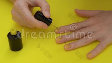 一个女孩在黄色背景下把指甲涂成黄色的特写镜头。 黄色概念。
